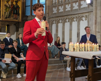 Ein Junge steht in einer Kirche und hält eine Kerze und ein Mikro