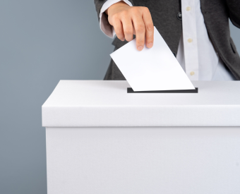 Ein Mensch steckt einen Wahlzettel in eine Wahlurne