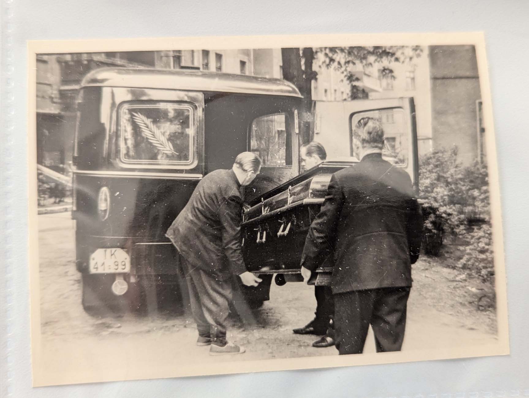 Foto, auf dem zwei Männer einen Sarg in ein Auto laden